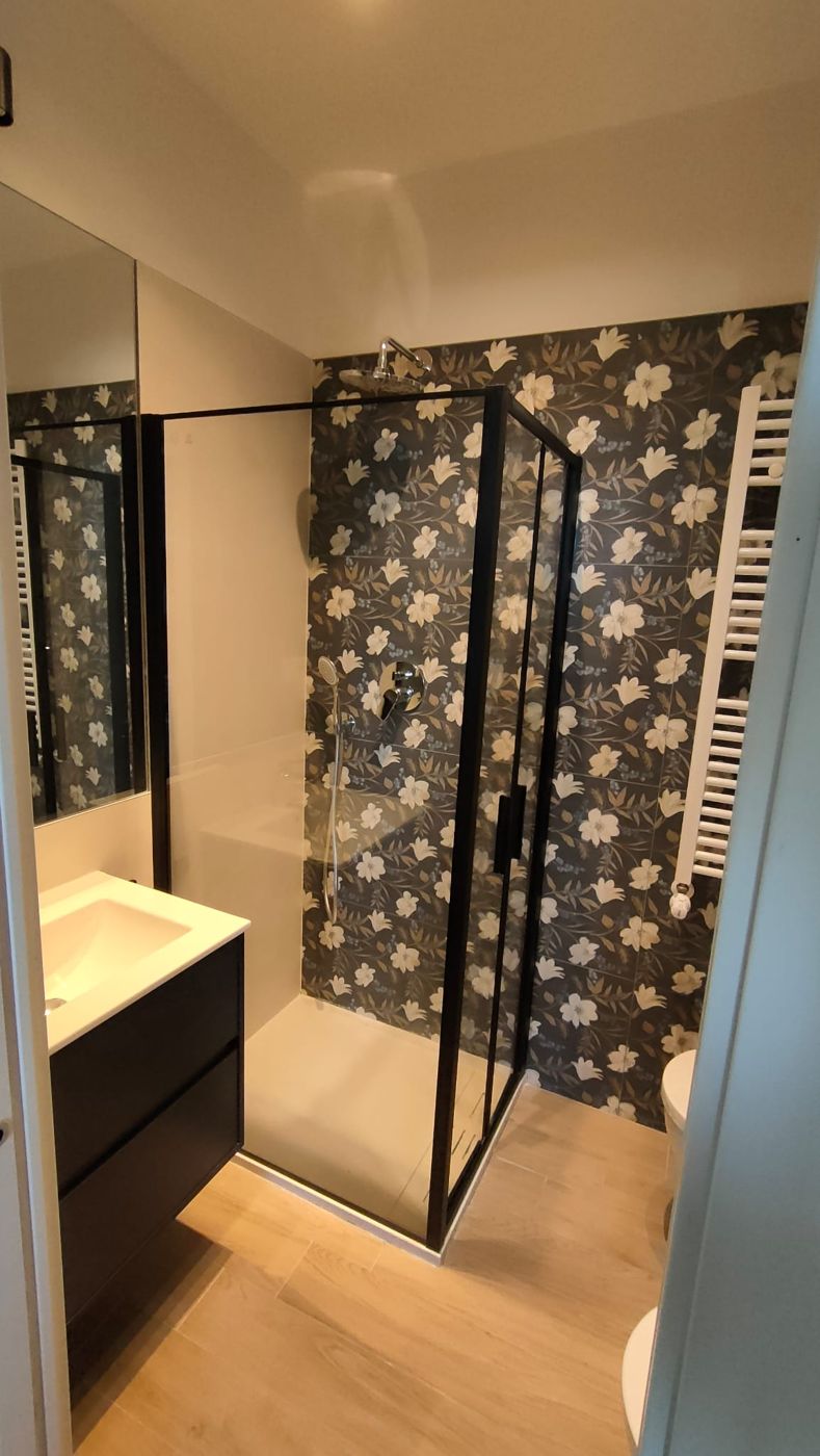 Bagno con piastrelle a fiori su fondo scuro, box doccia nero e mobile lavabo scuro
